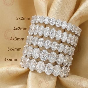 Op de afbeelding: Zes diamanten eternity ringen met verschillende ovale steenmaten, gepresenteerd op gouden stof. Maten: 3x2mm, 4x2mm, 4x3mm, 5x4mm en 6x4mm. Elke ring heeft een doorlopende rij ovaal geslepen diamanten.