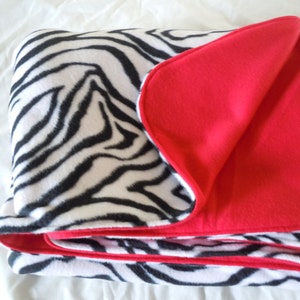 May include: A soft, cosy blanket with a zebra print on one side and a solid red fleece on the other side. The blanket is folded in half and the red side is facing up.
