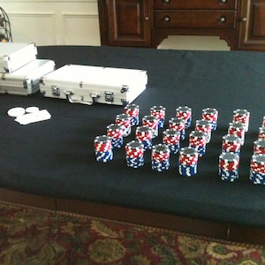 May include: A black felt-covered table with two silver aluminum cases and a row of red, white, and blue poker chips.