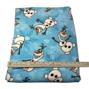May include: Blue fleece fabric with a repeating pattern of Olaf from the movie Frozen. The fabric is approximately 18 inches wide.