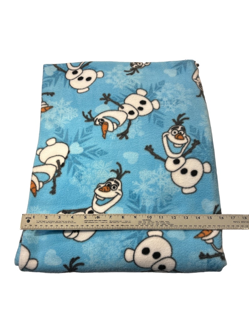 May include: Blue fleece fabric with a repeating pattern of Olaf from the movie Frozen. The fabric is approximately 18 inches wide.
