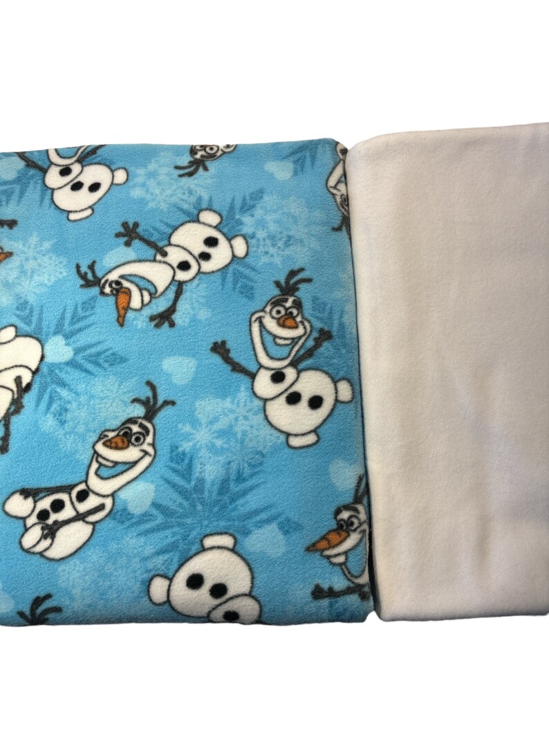 May include: A blue fleece blanket with a white fleece backing. The blue side features a repeating pattern of Olaf the Snowman from the movie Frozen.