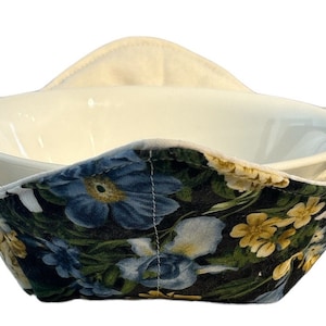 Puede incluir: Un calientaplatos floral con forro blanco y estampado floral azul oscuro y verde. El calientaplatos está diseñado para sujetar un cuenco y mantenerlo caliente.