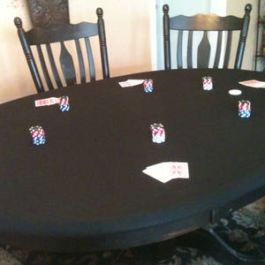 May include: A black felt-covered table with poker chips and playing cards scattered on the surface. Two wooden chairs are visible in the background.