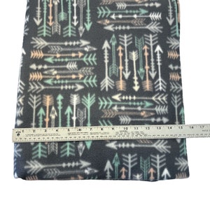 May include: A gray fleece fabric with a repeating pattern of white, green, and peach arrows. The fabric is measured with a ruler, showing it is 16 inches wide.