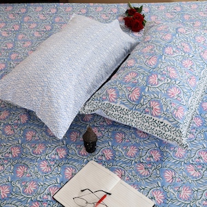 Peut inclure: Deux oreillers rectangulaires et un drap assorti présentant un fond bleu clair avec un motif répétitif de fleurs de lotus roses et de vignes vertes. Un oreiller affiche un motif dense et fin de vagues bleues et blanches.