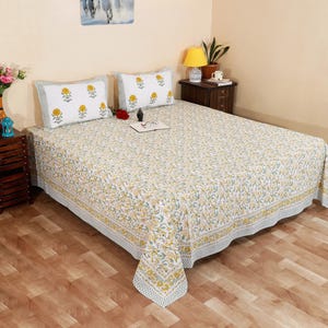 Puede incluir: Un edredón con estampado floral y dos fundas de almohada a juego. La ropa de cama blanca presenta un diseño floral amarillo y verde. Las fundas de almohada tienen un estampado de flores amarillas con un borde verde. El edredón tiene un borde estampado.