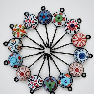 May include: A collection of decorative ceramic cabinet knobs with various colorful floral and geometric patterns. Each knob is attached to a black metal stem. The knobs are arranged in a circular pattern against a white background.