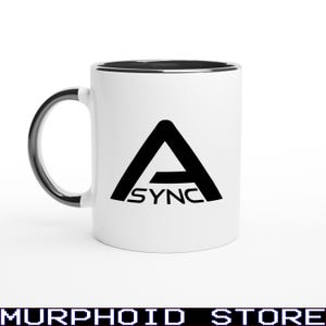 Puede incluir: Una taza de cerámica blanca con interior y asa de color negro. La parte frontal de la taza presenta un logotipo gráfico negro que consiste en una gran forma triangular con el texto ASYNC impreso en una fuente sans-serif en negrita.