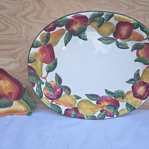 May include: Oval ceramic serving platter and matching pear-shaped dish. The platter has a white center with a border of red apples, yellow pears, and green leaves. The pear-shaped dish is painted with similar colors.