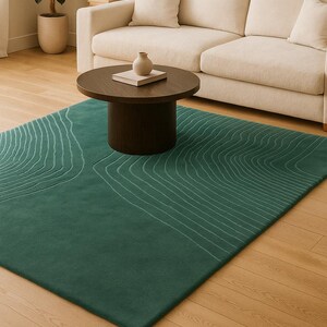 May include: A rectangular, emerald green rug with a topographic design in light green lines. The rug is placed on a hardwood floor, with a dark brown coffee table and a beige sofa in the background. A small vase and a book are on the table.