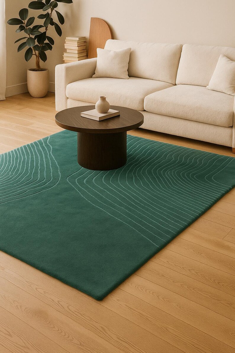 May include: A rectangular, emerald green rug with a topographic design in light green lines. The rug is placed on a hardwood floor, with a dark brown coffee table and a beige sofa in the background. A small vase and a book are on the table.