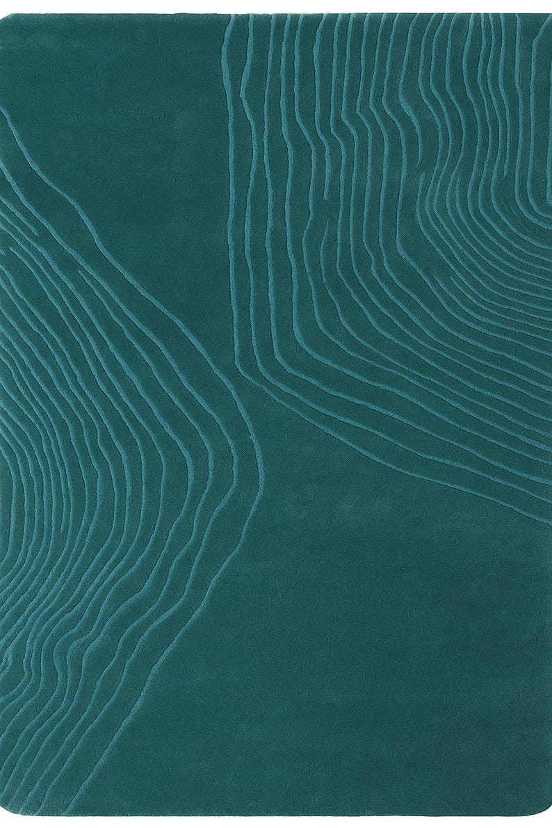 May include: Teal-colored rug with a textured design. The rug features a pattern of curved, parallel lines in a lighter shade of teal, creating a topographic effect. The design covers a large portion of the rug's surface, adding visual interest.