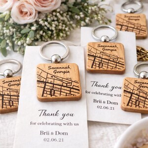 May include: Wooden keychains engraved with a map of Savannah, Georgia, with silver key rings. Each keychain is square and features a detailed street map design. The keychains are displayed with cards that read "Thank you" and the names "Brii & Dom" and the date "02.06.21".