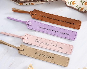 May include: Four leather bookmarks in shades of brown, lavender, pink, and tan. Each bookmark has a leather loop and stitched edges. Text on the bookmarks includes: "A reader lives a thousand lives", "To many more chapters", "Find your story", and a date.