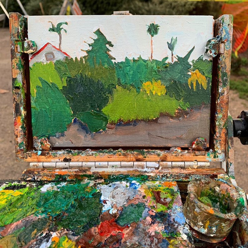 K&ouml;nnte beinhalten: &Ouml;lgem&auml;lde einer Landschaft mit Haus, B&auml;umen und Stra&szlig;e. Das Kunstwerk wird auf einer h&ouml;lzernen Staffelei pr&auml;sentiert, zusammen mit einer bunten K&uuml;nstlerpalette und einem kleinen Farbbeh&auml;lter.