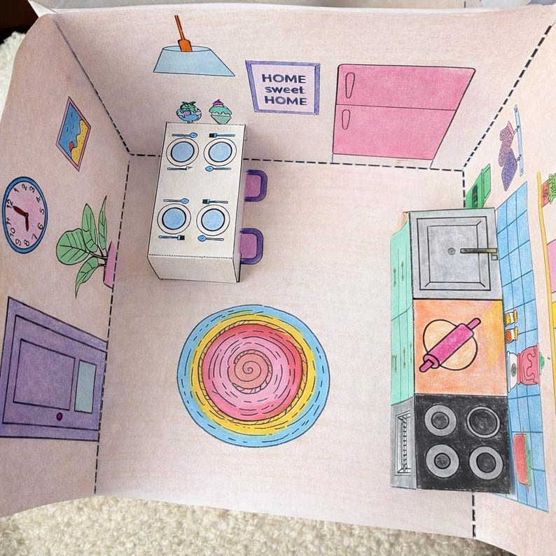 May include: A colorful, hand-drawn paper dollhouse kitchen scene. The kitchen features a stove, refrigerator, and cabinets. A table is set with plates and silverware. The words "HOME sweet HOME" are displayed on the wall. A round rug is on the floor.