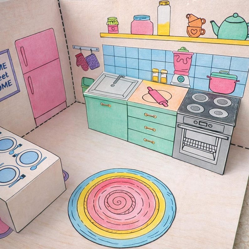 May include: A colorful papercraft kitchen scene with a pink refrigerator, teal cabinets, and a stove. The kitchen includes a sink, blender, and a rolling pin. A round rug with pink, yellow, and blue spirals sits on the floor.