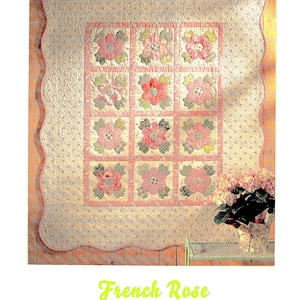 Puede incluir: Una colcha floral rosa y verde con un borde festoneado. La colcha está colgada en una pared de madera y dice "French Rose Lap Quilt".