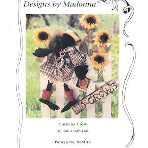 May include: A black and white checkered cloth doll with red boots and a black hat, standing on a white picket fence with sunflowers and a sign that says "No Crows". The doll is 18 inches tall and is called "Cornelia Crow".