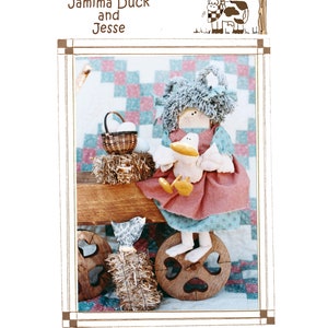May include: A Homespun Farms design featuring a doll with blue hair and a pink dress holding a yellow duck. The doll is sitting on a wooden wheel with a heart-shaped cutout. The doll is surrounded by hay and a basket of eggs.
