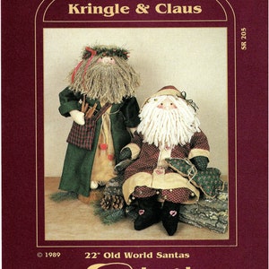 May include: A sewing pattern for two 22-inch Old World Santa dolls, one with a green robe and a white beard, and the other with a red and white robe and a white beard. The pattern is from "my sister & i PATTERNS" and is titled "Kringle & Claus".