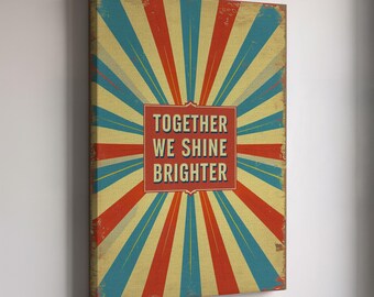 May include: A rectangular canvas print with a vintage design. The background features a burst of red, blue, and yellow rays. A red square in the center contains the text "TOGETHER WE SHINE BRIGHTER" in white. The print has a distressed, aged appearance.