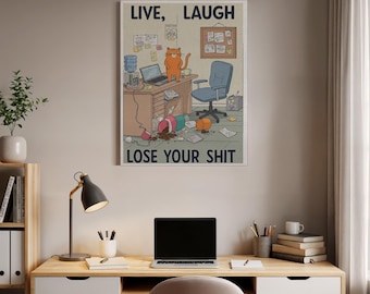 May include: A framed poster with the text "LIVE, LAUGH, LOSE YOUR SHIT" above a cartoon illustration of a messy office. The illustration features a desk with a laptop, a cat, and scattered items. A blue office chair is also visible.