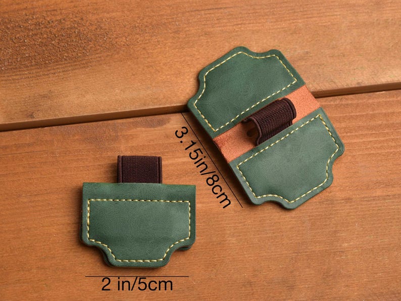 May include: Two green leather pen holders with brown elastic bands and tan leather accents. The pen holders are 2 inches (5 cm) wide and 3.15 inches (8 cm) long. The edges are stitched with yellow thread.