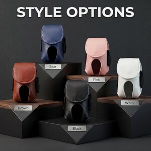 May include: Five small, structured cases with flap closures and cut-out bottoms, displayed in blue, brown, pink, black, and white. Each case features visible stitching and is labeled with its respective color on a small metal plaque.