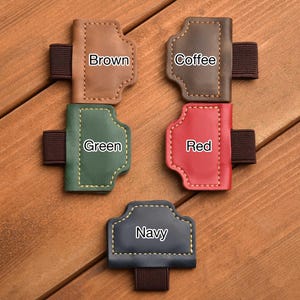 May include: A collection of leather pen holders in various colors: brown, coffee, green, red, and navy. Each holder has a stitched design and an elastic band. The colors are labeled on each holder.