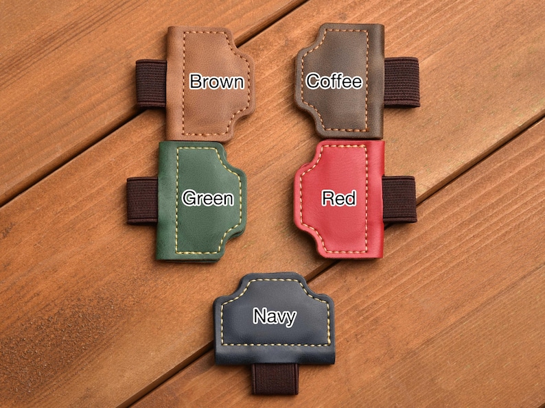 May include: A collection of leather pen holders in various colors: brown, coffee, green, red, and navy. Each holder has a stitched design and an elastic band. The colors are labeled on each holder.