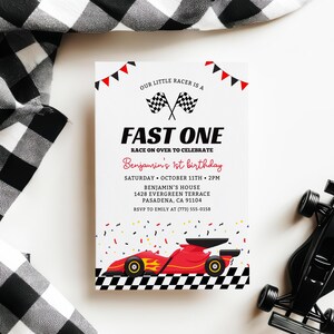 Puede incluir: Una tarjeta de invitación blanca con el texto "FAST ONE" y "Benjamin's 1st birthday". La tarjeta presenta un gráfico de coche de carreras rojo y banderas a cuadros. Un coche de carreras de juguete negro está al lado de la tarjeta.