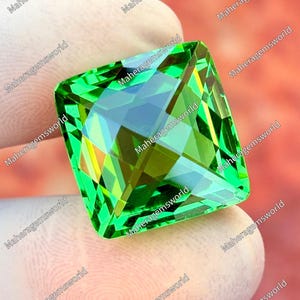 Könnte beinhalten: Ein großer, quadratisch geschliffener, facettierter Edelstein mit leuchtend grüner Farbe. Der Edelstein hat eine komplexe innere Struktur, die das Licht reflektiert und eine schillernde Darstellung erzeugt. Der Stein wird von einer behandschuhten Hand gehalten.