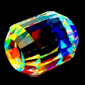 May include: A faceted, cylindrical object with a vibrant display of colors. The object's surface is a mosaic of geometric shapes, reflecting hues of red, yellow, blue, and green against a black background. The overall effect is a dazzling, prismatic display.