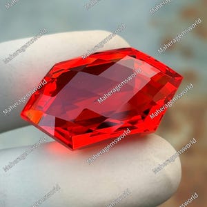May include: A vibrant, faceted, shield-shaped red gemstone with a brilliant cut. The stone displays intense saturation and clarity, featuring multiple geometric facets that reflect light across its surface, creating a sharp, angular, and symmetrical appearance.