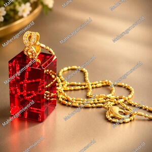 Peut inclure: Un pendentif doré avec un symbole infini orné de petites pierres claires, fixé sur un bloc de verre rouge rectangulaire. Une chaîne à billes dorée avec un fermoir mousqueton est reliée au pendentif et repose à côté du verre rouge.