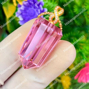 May include: A faceted pink crystal pendant shaped like a pointed prism, suspended from a gold-toned metal bail featuring an infinity symbol design encrusted with small clear stones, attached to a delicate gold-toned beaded chain.
