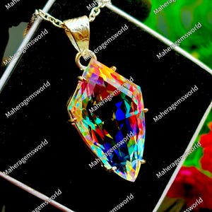 May include: A faceted, kite-shaped iridescent gemstone pendant set in a gold-toned metal frame. The stone displays a spectrum of vibrant colors including blue, yellow, and red. It hangs from a matching gold-toned chain, presented on a black display.