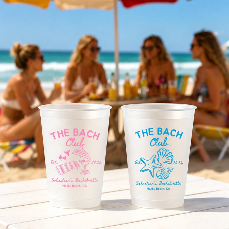 May include: Two white plastic cups with the text "THE BACH Club" in pink and blue, with beach-themed graphics. The cups are for Sebastian's Bachelorette in Malibu Beach, CA, with the year 2026. The background shows a beach scene.