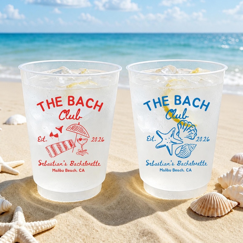 May include: Two clear plastic cups filled with a beverage and ice, with the text "THE BACH Club" in red and blue. The cups are decorated with beach-themed graphics and the text "Sebastian's Bachelorette Malibu Beach, CA". The cups are on a sandy beach.