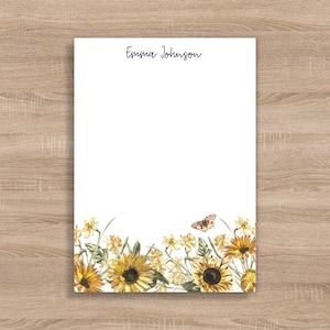 May include: White stationery with the name "Emma Johnson" in black script at the top. The bottom of the stationery features a watercolor design of sunflowers, other yellow flowers, and a butterfly.