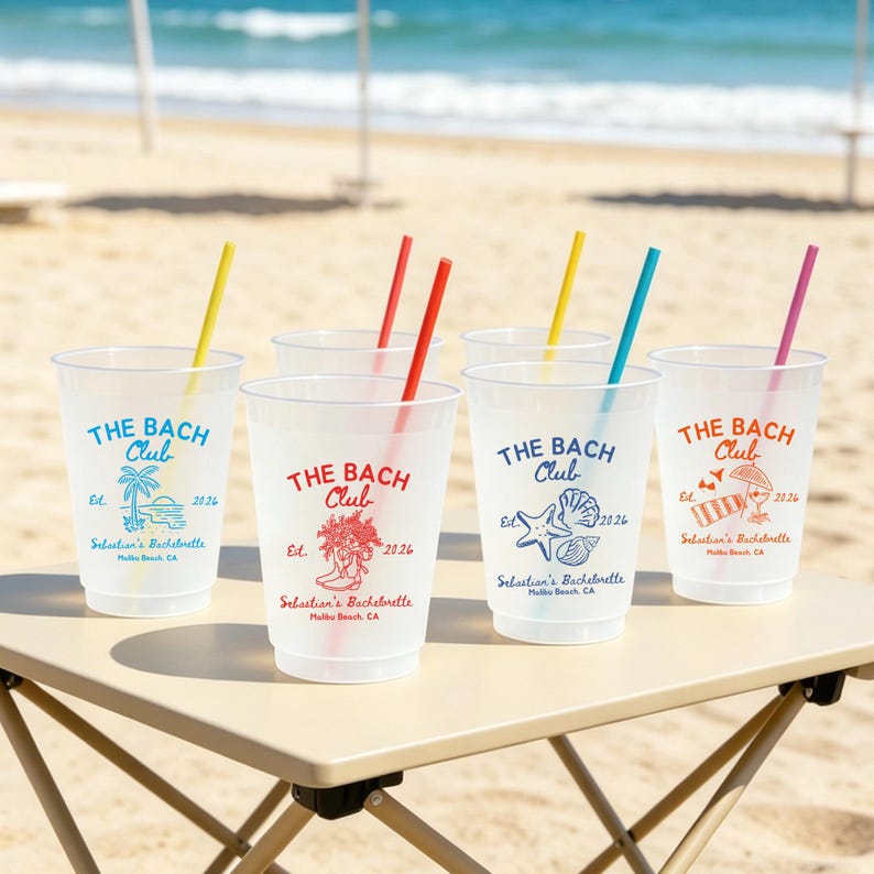 May include: Clear plastic cups with colorful straws are arranged on a table at the beach. Each cup is printed with "THE BACH Club" and a unique graphic, along with "Sebastian's Bachelorette" and the year 2026.