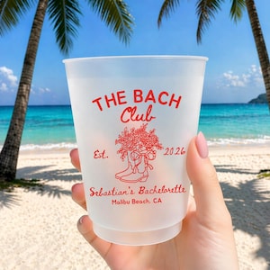 May include: A frosted plastic cup with red text that reads "THE BACH Club" and "Sebastian's Bachelorette Malibu Beach, CA". The cup has a floral and boot design and the year 2026. The background shows a beach with palm trees and blue water.