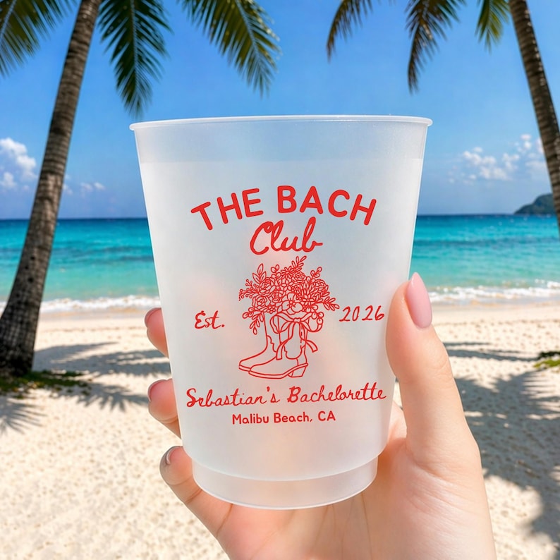 May include: A frosted plastic cup with red text that reads "THE BACH Club" and "Sebastian's Bachelorette Malibu Beach, CA". The cup has a floral and boot design and the year 2026. The background shows a beach with palm trees and blue water.