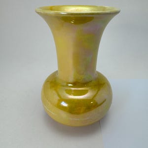 May include: A yellow iridescent vase with a bulbous base and flared rim. The vase has a glossy finish with subtle color variations. The overall shape is reminiscent of a tulip, suitable for displaying flowers or as a decorative piece.