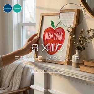 May include: A wooden 20x25 cm frame mockup featuring a red apple drawing with "New York City" text. The frame is held by a hand. The frame is displayed on a white surface.
