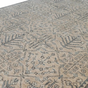 May include: Beige and gray patterned area rug. The rug features a repeating design of stylized floral and leaf motifs in shades of gray and blue against a beige background. The rug has a border in a darker gray.
