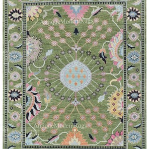 May include: A rectangular, green rug with an intricate floral design. The rug features a central medallion and a border with repeating floral patterns in shades of pink, blue, and orange. The text "Antique Modern Rugs" is visible on the rug.