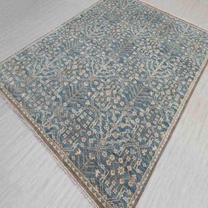 Pode incluir: Um tapete retangular azul com um padrão intrincado e repetitivo de formas geométricas e motivos florais bege e castanhos. O tapete tem uma borda castanha e uma borda com franjas, ideal para sala de estar ou quarto, aprox. 200 cm x 300 cm.